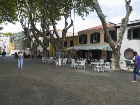Photo for Machico, Madeira, Portugal, May 17, 2022: Pedestrian street at center of Machico town with plane trees and houses at traditional portuguese colonial style - Royalty Free Image