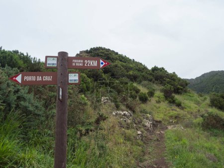 Collines verdoyantes et prairie avec sentier pédestre et panneau touristique pointant Porto da Cruz dans une direction et Percurso de treino à Machico dans l'autre