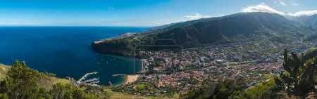Panoramic aerial view of Machico bay with golden sand beach, palm trees from Pico do Facho viewpoint over the Machico valley, Airport in the background, Madeira, Portugal.