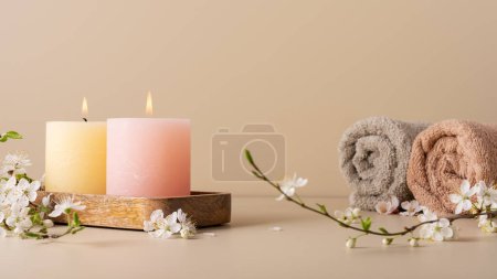 Téléchargez les photos : Bougies ardentes diffusant l'arôme sur la table dans une salle de spa. Belle composition avec des bougies de couleur pastel et perruque de fleur de cerisier pour le traitement spa, printemps. - en image libre de droit