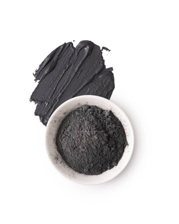 Cosmetic black clay powder in white ceramic bowl with a smear isolated on a white background