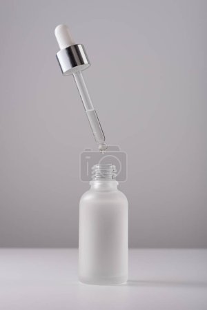 Serum bottle with pipette on gray background. Close-up frosted glass container for skin care beauty product.