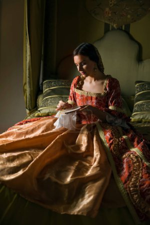 Foto de Dormitorio medieval de oro con hermosa cama con dosel. Una dama en vestido renacentista haciendo bordados. - Imagen libre de derechos