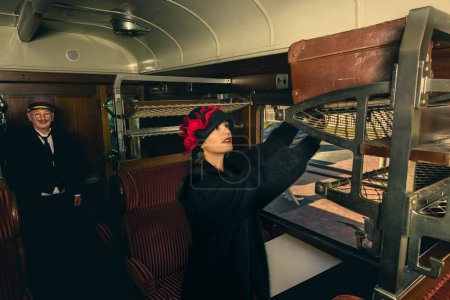 Photo for 1920s woman in flapper dress and cloche hat trying to store her old leather suitcase in a storage rack of the 1st class compartment - Royalty Free Image