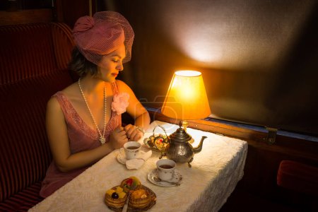 Photo for Reenactment scene of a 1920s flapper dress lady enjoying high tea in an authentic 1927 steam train compartment - Royalty Free Image