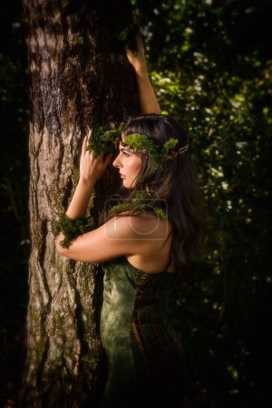 Téléchargez les photos : Belle jeune femme en robe verte se faisant passer pour une fée de la forêt avec des tissus en mousseline de soie pure et des guirlandes de mousse - en image libre de droit
