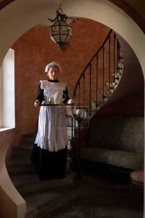 Foto de Criada victoriana o sirvienta en vestido negro, gorra de encaje y delantal blanco trabajando en un interior del siglo XIX - Imagen libre de derechos