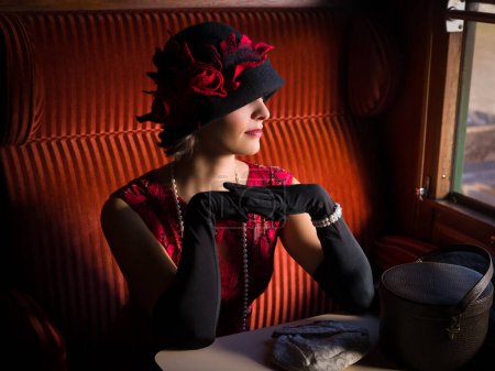 Téléchargez les photos : Attractive 1920s woman  in red flapper dress and cloche hat posing in the 1927 first class interior of an authentic steam train - en image libre de droit