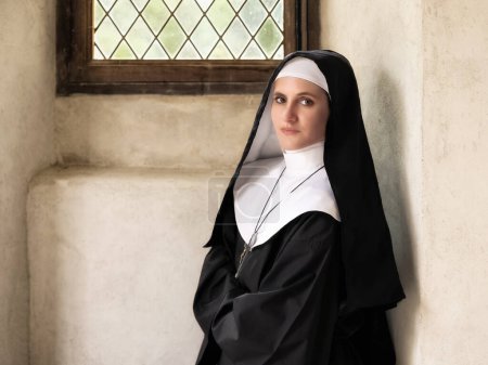 Photo for Young adult woman dressed in authentic habit and veil of a catholic nun in a medieval chapel - Royalty Free Image