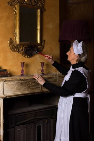 Téléchargez les photos : Servante victorienne ou servante en robe noire, bonnet en dentelle et tablier blanc travaillant à l'intérieur du XIXe siècle - en image libre de droit