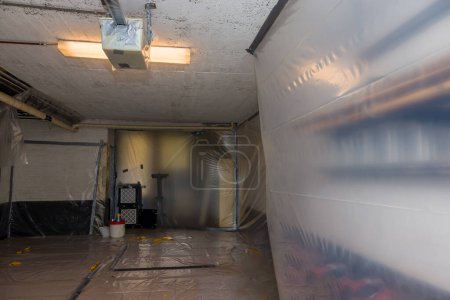 Téléchargez les photos : Enlèvement de l'amiante fonctionne hors des tuyaux de chauffage isolation en cours dans un sous-sol avec tous les murs recouverts de plastique et d'extraction d'air filtré pour enlever très fibre - en image libre de droit