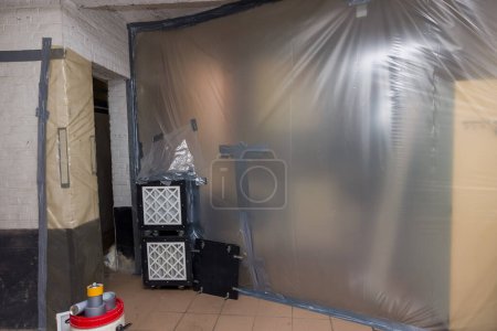 Photo for Asbestos removal works off heating pipes insultation going on in a basement with all walls covered in plastic and filtered air extraction to remove very fiber - Royalty Free Image