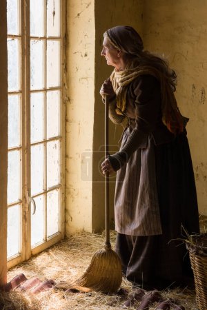 Téléchargez les photos : Femme en costume médiéval historique travaillant avec un balai dans un hangar à foin - en image libre de droit