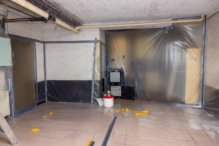Téléchargez les photos : Enlèvement de l'amiante fonctionne hors des tuyaux de chauffage isolation en cours dans un sous-sol avec tous les murs recouverts de plastique et d'extraction d'air filtré pour enlever très fibre - en image libre de droit