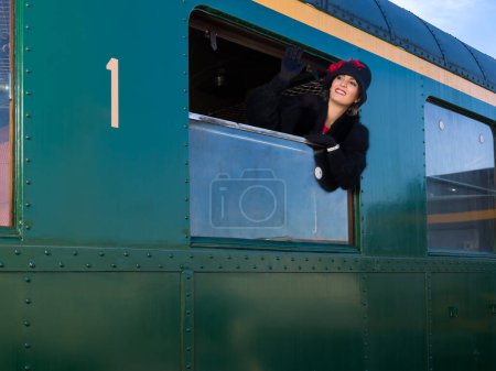 Téléchargez les photos : Femme des années 1920 vêtue d'un manteau de fourrure et d'un chapeau cloche accrochés par la fenêtre d'un wagon de train antique - en image libre de droit