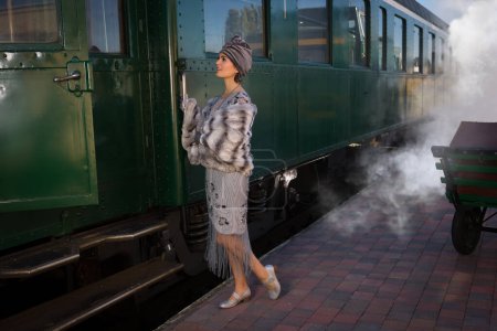 Téléchargez les photos : Dame dans les années 1920 robe battant costume attendant le train à vapeur sur une plate-forme de train - en image libre de droit
