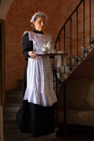 Foto de Criada victoriana o sirvienta en vestido negro, gorra de encaje y delantal blanco trabajando en un interior del siglo XIX - Imagen libre de derechos