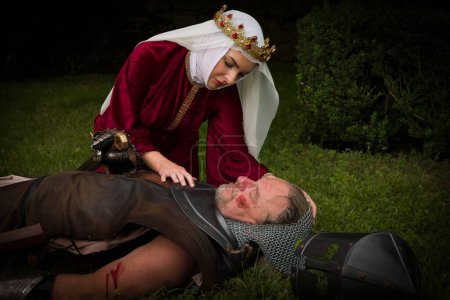 Foto de Escena medieval de una joven reina viuda llorando arrodillada junto a un caballero muerto caído en el campo de batalla - Imagen libre de derechos
