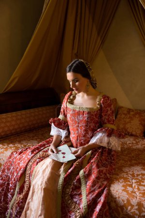 Renaissance lady in late medieval gown sitting on a beautiful canopy bed in her castle bedroom