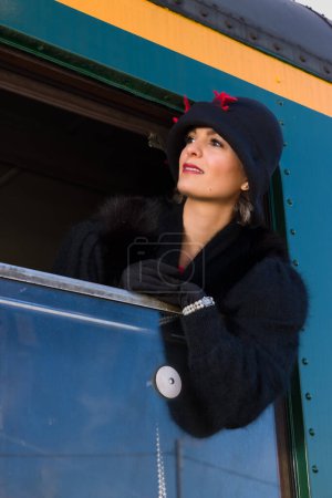 Téléchargez les photos : Femme des années 1920 vêtue d'un manteau de fourrure et d'un chapeau cloche accrochés par la fenêtre d'un wagon de train antique - en image libre de droit