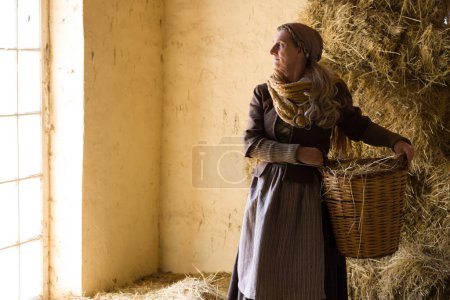 Woman in historical medieval costume posing with a wicker basket in a hay barn
