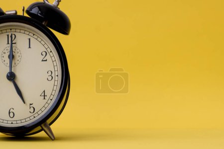 Foto de Analog alarm clock displaying five o'clock on a yellow background with copy space. Vintage and retro feel. - Imagen libre de derechos
