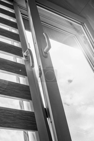Foto de Una ventana de plástico abierta para la ventilación con una persiana enrollable y una mosquitera contra el cielo azul - Imagen libre de derechos