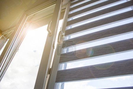 Foto de Una ventana de plástico abierta para la ventilación con una persiana enrollable y una mosquitera contra el cielo azul - Imagen libre de derechos