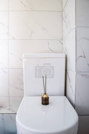 Foto de Ambientador de aire con palos de pie en un inodoro de mármol en un baño blanco limpio - Imagen libre de derechos