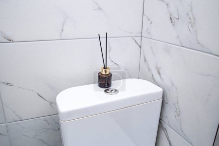 Foto de Ambientador de aire con palos de pie en un inodoro de mármol en un baño blanco limpio - Imagen libre de derechos