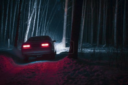 Sportwagen mit eingeschaltetem Fernlicht in einem Winter-Kiefernwald bei Nacht, Front und Hintergrund mit Bokeh-Effekt verschwommen 