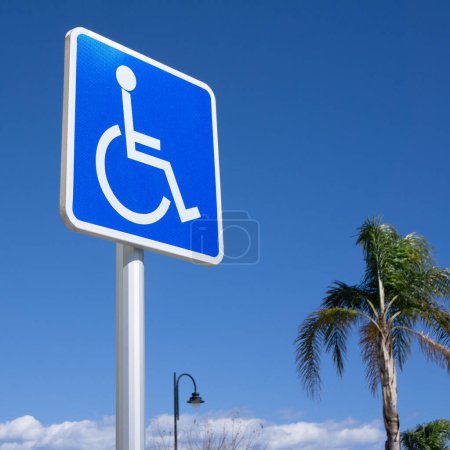 Téléchargez les photos : Panneau de stationnement bleu pour handicapés avec ciel bleu, palmier, poteau lumineux et nuages - en image libre de droit