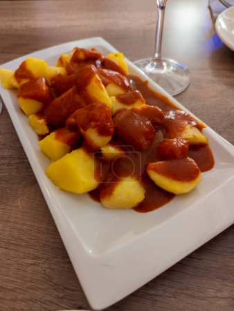 Foto de Plato típico español llamado patatas bravas, tubérculos fritos con salsa picante roja que contiene cebolla, pimentón, orégano, chile - Imagen libre de derechos