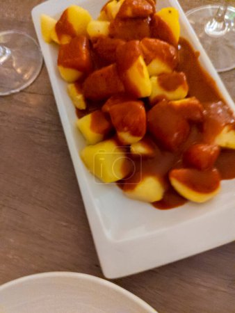 Foto de Plato típico español llamado patatas bravas, tubérculos fritos con salsa picante roja que contiene cebolla, pimentón, orégano, chile - Imagen libre de derechos
