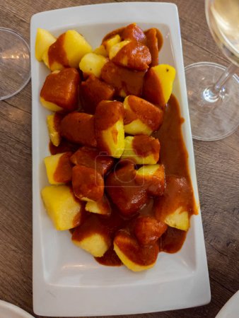 Téléchargez les photos : Plat espagnol typique appelé patatas bravas, tubercules frits à la sauce épicée rouge contenant de l'oignon, paprika, origan, piment - en image libre de droit
