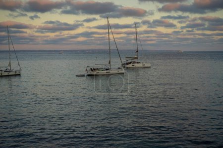 Foto de Barcas de recreo se encuentran ancladas en una cala de Mallorca, disfrutando del abrazo ámbar de la puesta del sol, capturando la esencia de la tranquilidad balear. - Imagen libre de derechos
