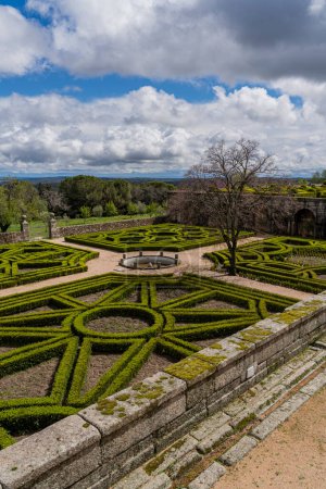 Téléchargez les photos : Les jardins du monastère royal El Escorial arborent des haies géométriques précises dans un décor pittoresque, sous le ciel spectaculaire de Madrid - en image libre de droit