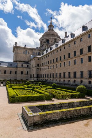 Los jardines del Real Monasterio de El Escorial muestran precisos setos geométricos sobre un escenario escénico, bajo el dramático cielo madrileño