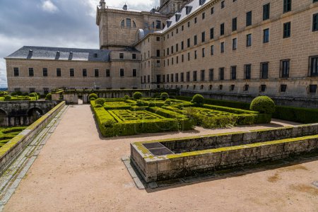 Téléchargez les photos : Les jardins du monastère royal El Escorial arborent des haies géométriques précises dans un décor pittoresque, sous le ciel spectaculaire de Madrid - en image libre de droit