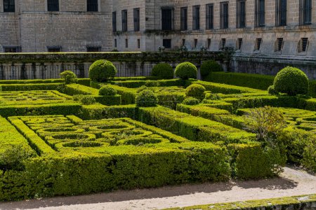 Los jardines del Real Monasterio de El Escorial muestran precisos setos geométricos sobre un escenario escénico, bajo el dramático cielo madrileño