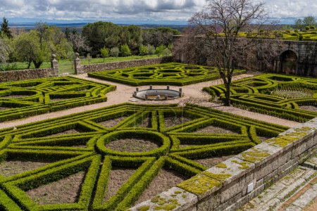 Foto de Los jardines del Real Monasterio de El Escorial muestran precisos setos geométricos sobre un escenario escénico, bajo el dramático cielo madrileño - Imagen libre de derechos