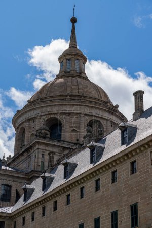 Téléchargez les photos : Les détails sculpturaux et le dôme emblématique du monastère El Escorial se distinguent par un ciel bleu avec des nuages duveteux - en image libre de droit