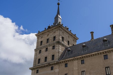 Foto de Los detalles escultóricos y la icónica cúpula del Monasterio de El Escorial destacan sobre un cielo azul con nubes esponjosas - Imagen libre de derechos