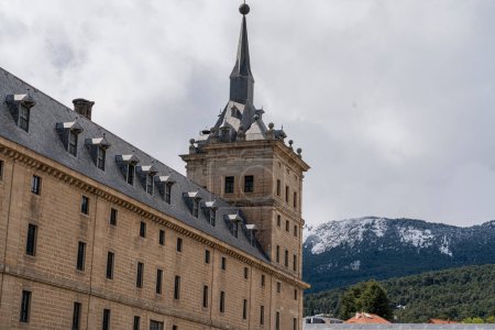 Sculptural details and the iconic dome of El Escorial Monastery stand out against a blue sky with fluffy clouds