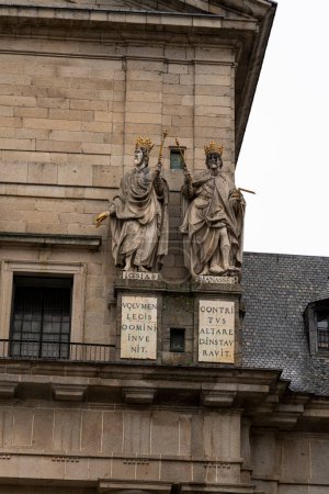 Foto de Estatuas doradas de reyes bíblicos adornan la fachada del Monasterio de El Escorial, colocadas contra las paredes de piedra y placas inscritas. - Imagen libre de derechos