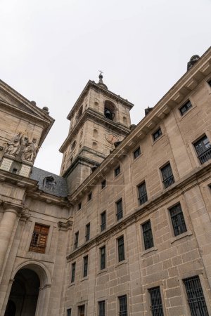 Statuen historischer Persönlichkeiten stehen über dem Haupthof des El Escorial-Klosters, vor der strengen Eleganz der Fassade des Gebäudes.