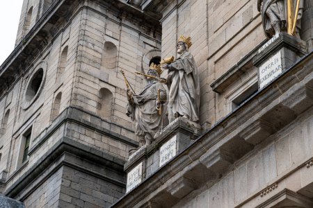Téléchargez les photos : Des statues dorées de rois bibliques ornent la façade du monastère El Escorial, dressées contre les murs pierreux et les plaques inscrites. - en image libre de droit