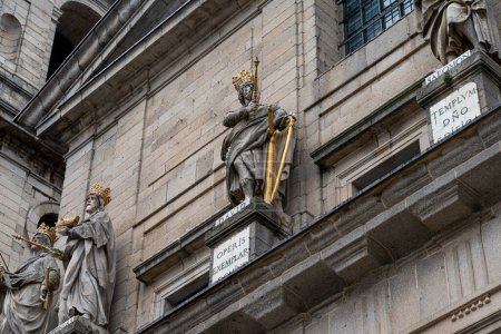 Gilded statues of biblical kings adorn the facade of El Escorial Monastery, set against the stony walls and inscribed plaques.