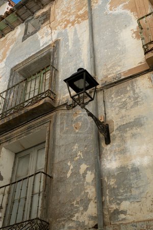 An old street lamp hangs from a building with peeling paint, highlighting the rustic charm of urban decay.