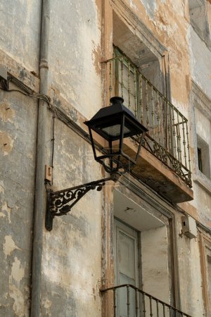 Foto de Una vieja lámpara de calle cuelga de un edificio con pintura pelada, destacando el encanto rústico de la decadencia urbana. - Imagen libre de derechos